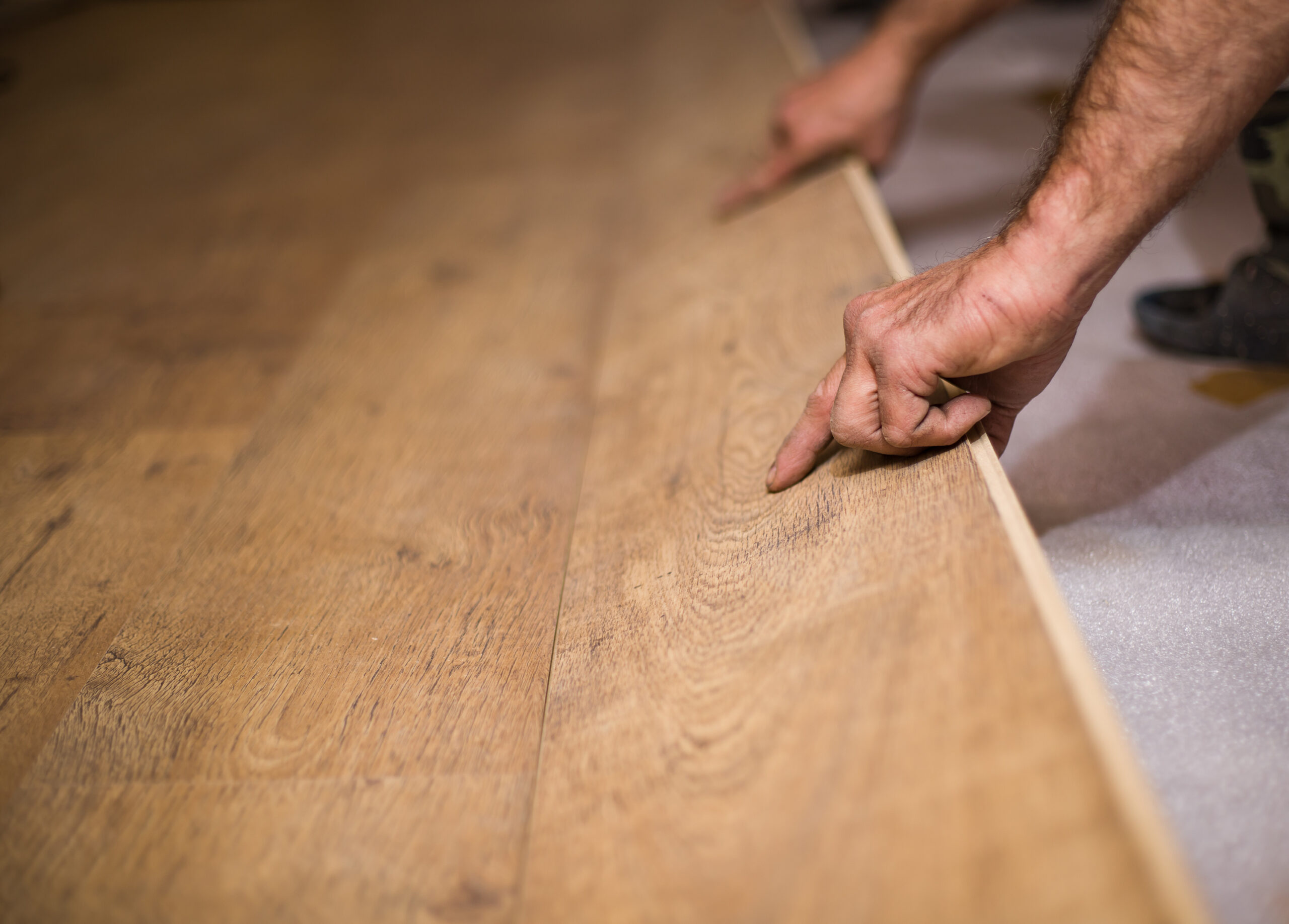 Man laying laminate flooring, top view, closeup on hands, no person.